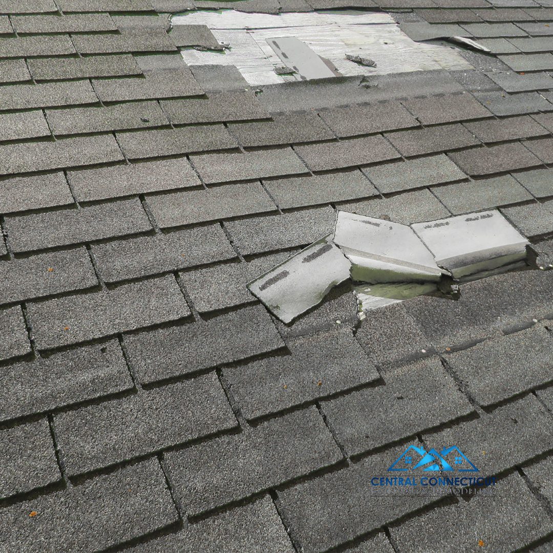 Close-up of a residential roof in Connecticut with missing and damaged shingles after a storm, exposing the underlayment beneath.